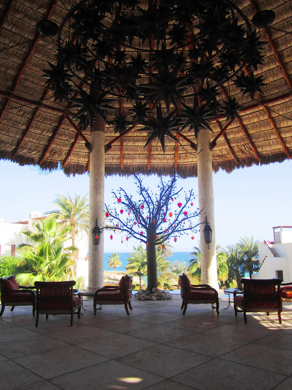 Outdoor patio at a resort in Mexico with a large black sunburst chandelier, armchairs, tile floor and a tree holding red, glass hearts