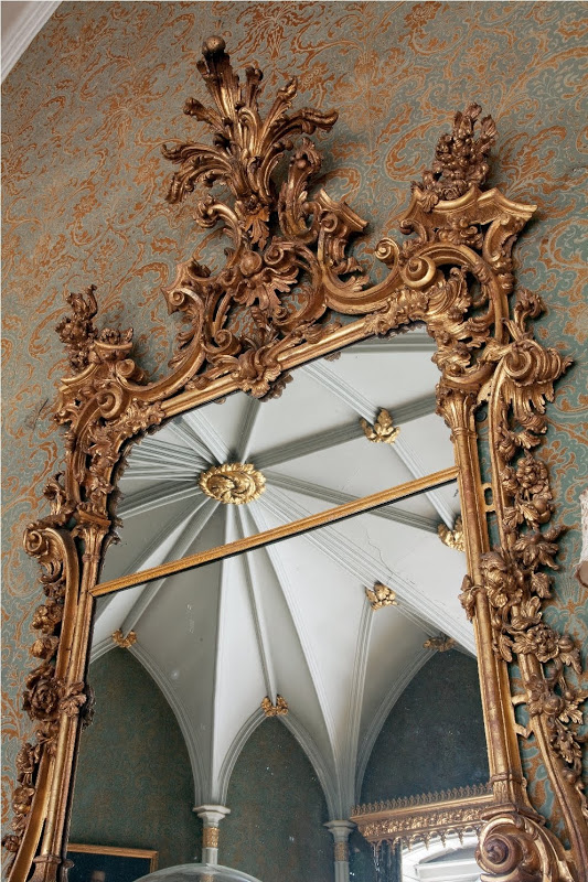 Mirror in a baroque gold frame reflecting a white vaulted ceiling with gold detailing