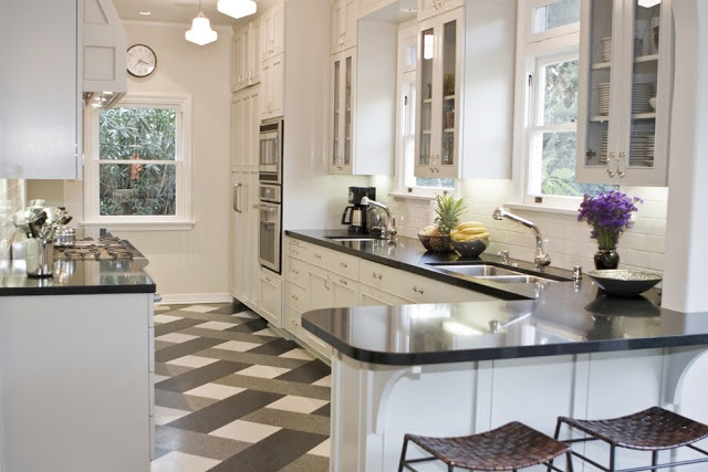 Tom Newman's kitchen in his Los Angeles home with a plaid floor, schoolhouse ceiling lights, stainless appliances, paneled cabinets, black counters and woven barstools