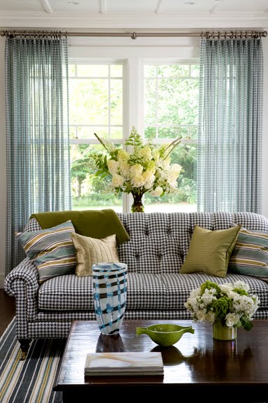 Living room with a tufted, black and white gingham sofa, striped rug, sheer gingham curtains and a wood coffee table