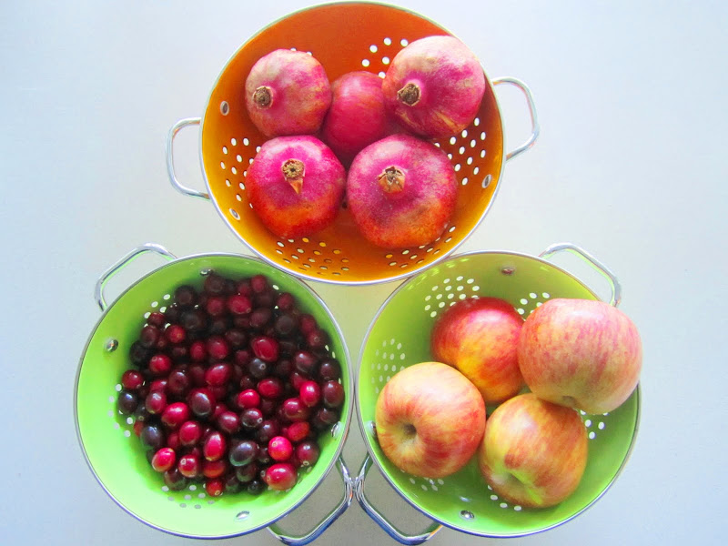 cranberries, pomegranates and apples in colanders on a white table