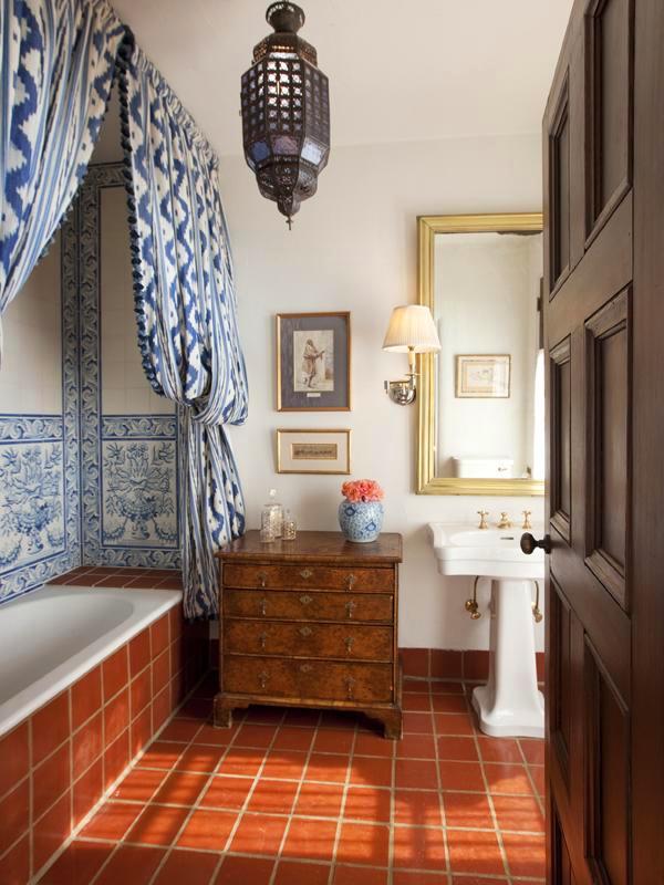Bathroom in a Montecito mansion with blue and white ikat curtains instead of a glass door to the tub, a built in tub with, blue and white Portuguese tile line the back wall, a pedestal sink, a wood chest of drawers and a Moroccan lantern light