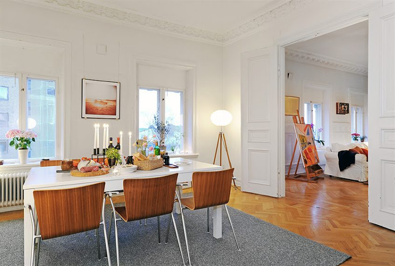 Kitchen in a Swedish apartment with herringbone wood floor, carved crown molding, the decorative ceiling medallions, tall paneled doors, grey rug and a white table surrounded by wood chairs with metal arms and legs