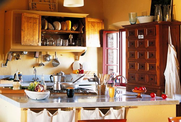 Warm Tuscan kitchen with yellow walls, wood cabinets, a large wooden chest of drawers, and blue grey countertops