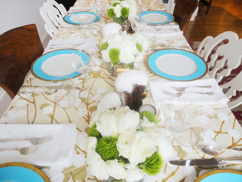 Holiday table setting with flower arrangements made of white Peonies, Ranunculus and green PomPoms, blossom tablecloth by Marimekko from Crate and Barrel, turquoise blue rimmed china, white ceramic pine cones and squirrels