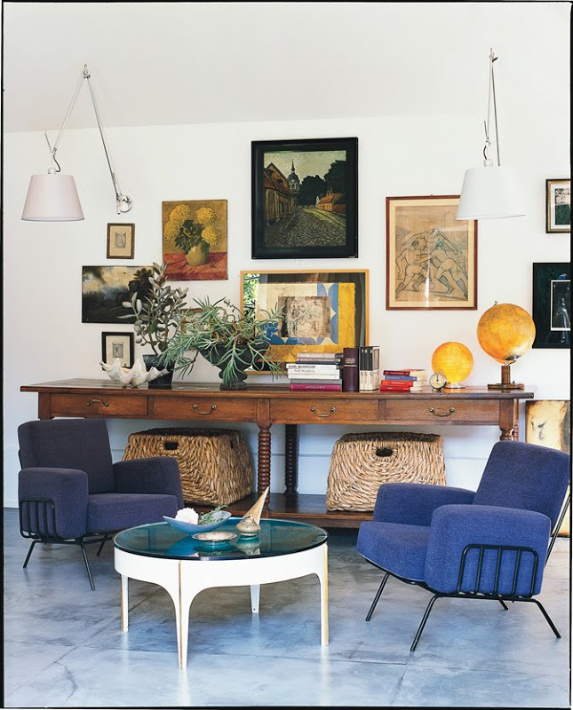 Den with blue tile floor and armchairs, a round coffee table, a long wood table with wicker baskets and two white wall mounted lights