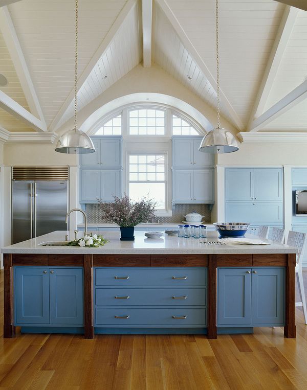 Kitchen with high vaulted ceilings, cornflower blue drawers and cabinets, wood floor, two nickle pendant lights,stainless appliances and an island with marble countertop