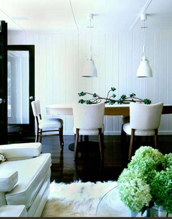 Dining room with dark wood floor, beadboard walls, two white pendant lights, wood chairs with white upholstered seats and backs and a sculptural centerpiece