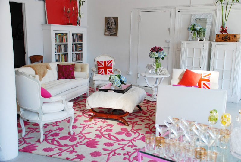 White living room in a NYC loft a tufted sofa, chaise lounge, upholstered Louis XIV chairs, an ottoman with wood legs on a pink and white area rug