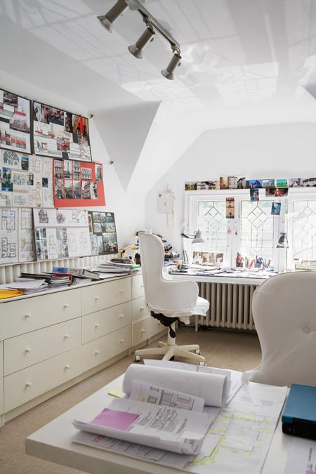 White attic home office with white drawers, two desks with white rolling armchairs,a window and a big bulletin board