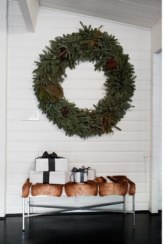 Foyer with dark wood floor, beadboard wall, a bench holding four presents and a large wreath