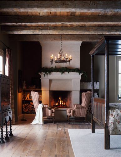 Bedroom with wood floor, exposed beams, a large fireplace with a festive holiday garland