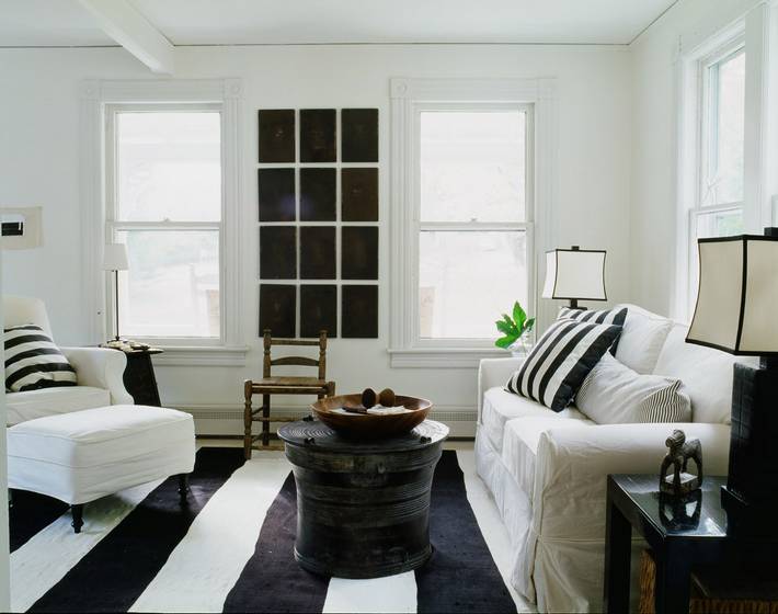 Alternative view of a living room in a cottage with black and white striped rug, white sofa, armchair and ottoman with black and white striped accent pillows, a black coffee table and a fake window 