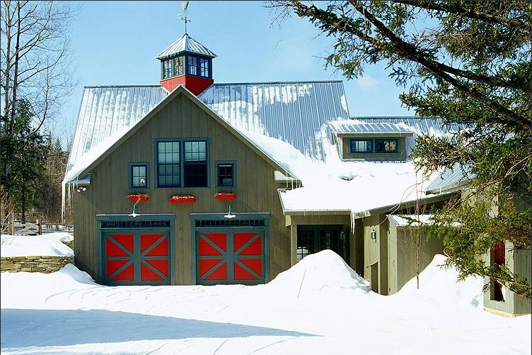 Exterior of a green barn with red and blue doors covered in snow