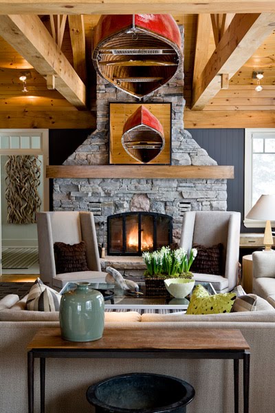 Living room in a cabin with knotty wood floor, grey sofa and armchairs with high backs, a flagstone fireplace, exposed beams and a red, upside down canoe hanging from the ceiling
