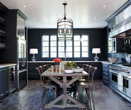 Eat in kitchen with dark cabinetry, cobellstons arraged like paver field tiles on the floor, white beadboard ceiling, a chandelier, a farmhouse table surrounded by matching chairs