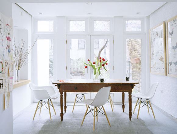 White dining room with eames chairs, large windows, a wood table, tulips and framed bird prints