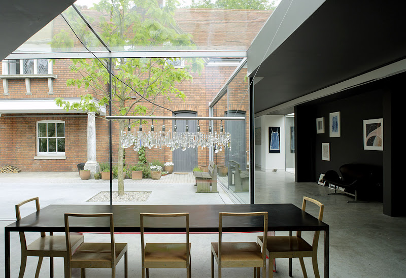 Kitchen with a glass wall and ceiling and a view of a courtyard, light bulb chandelier, and long dark table surrounded by wood chairs