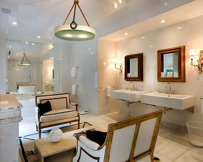 Bathroom with dueling settees, two wall mounted sinks, marble tile floor, a large mirror and an oval pendant light