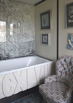 Bathroom with a large map on the wall, a step in tub with CCXLVIII written on the side, a blue and brown rug and a tufted armchair with a graphic brown, blue and white pattern