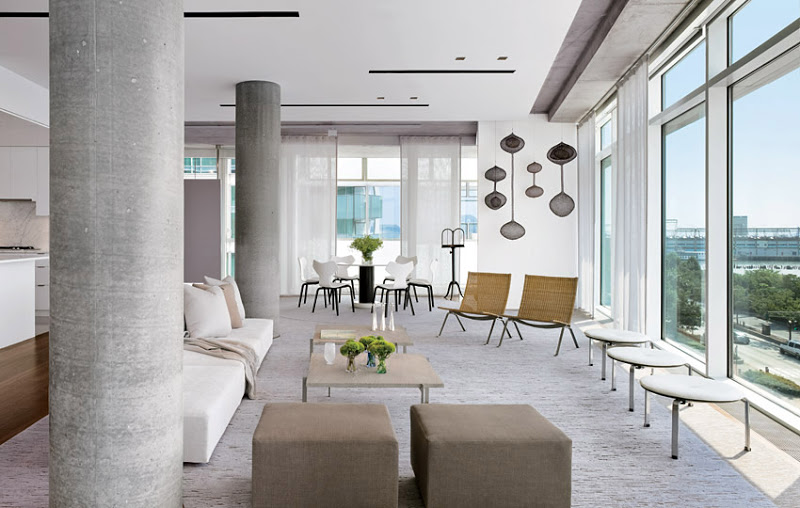 Modern living room in a NYC apartment with cement pillars, white sofa, grey cube ottomans, two armchairs. large picture windows and modern art hanging from the ceiling