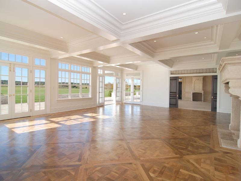 Empty living room in a Hamptons farm with coffered ceiling, large windows, wood floor and a massive fireplace