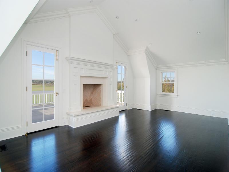 Empty bedroom in a Hamptons farm with dark wood floor, white walls, a fireplace and a door leading to an outdoor patio