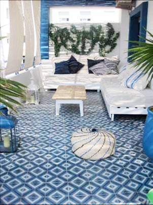 Patio with blue and white cement Moroccan tiles, white outdoor benches with white cushions and blue and white accent pillows