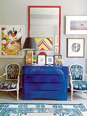 Bedroom with a Yves Klein blue dresser, two ikat print upholstered Louis XIV chairs, a blue and white rug and a large mirror in a red frame