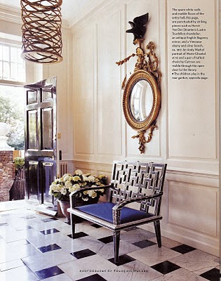 Foyer with black and white marble tile floor, an iron bench with Yves Klein blue cushion, paneled walls and a decorative mirror