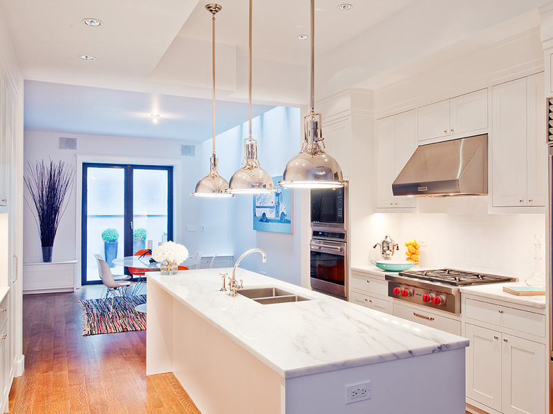 Open kitchen with three nickle pendant lights and marble counters in a LEED certified townhouse