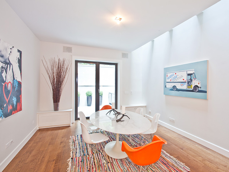 Dining room in a LEED certified townhouse with white tulip table, orange and white Eames chairs and a striped rug