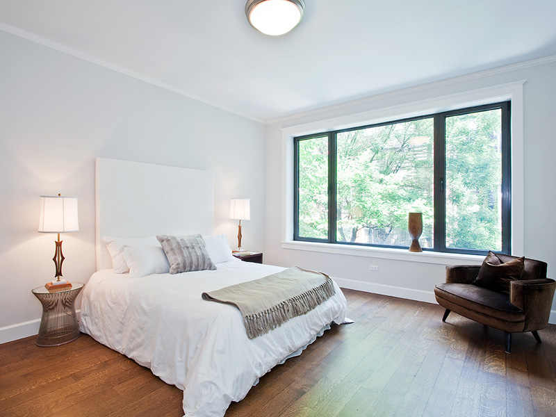 Master bedroom in a LEED certified townhouse with black paned windows and a tall white upholstered headboard