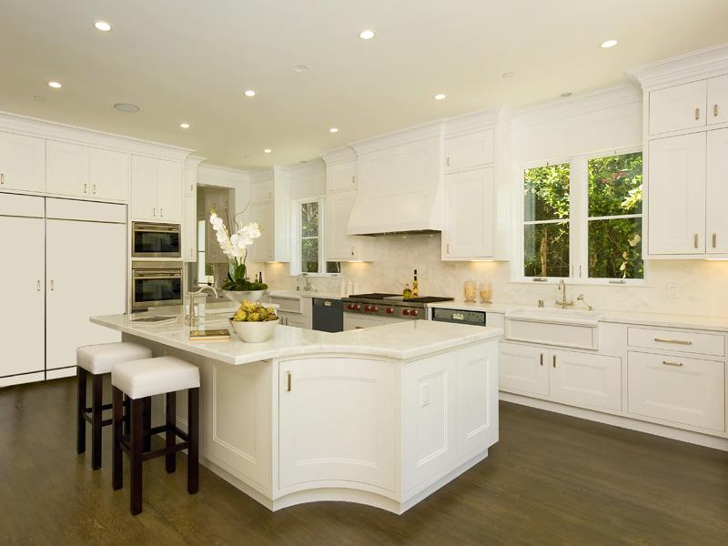 White kitchen with marble countertops, an island with two wood bar stools wiht white cushions and wood floor