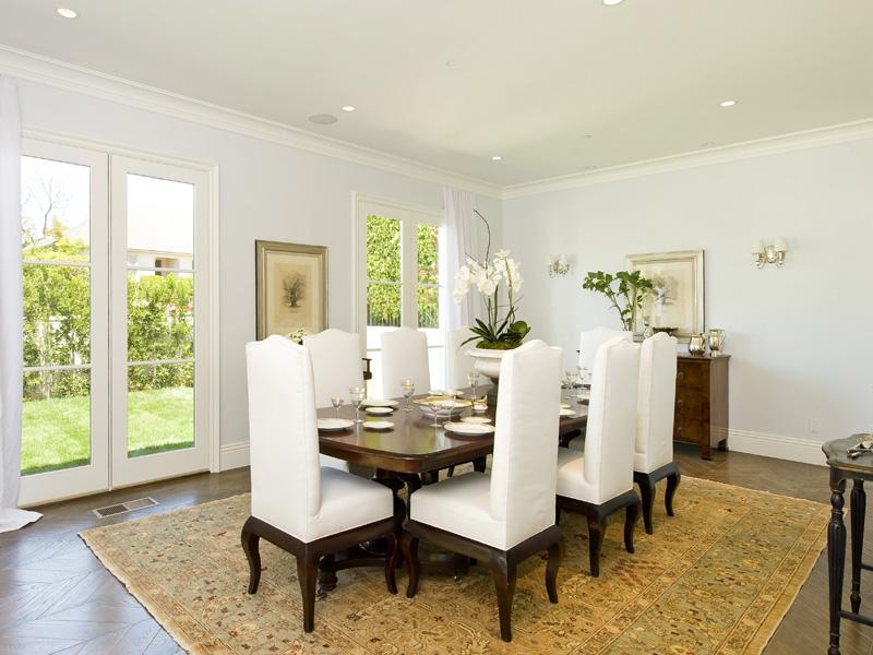 Formal dining room in an LA mansion with high back, white upholstered chairs and French doors leading to the backyard