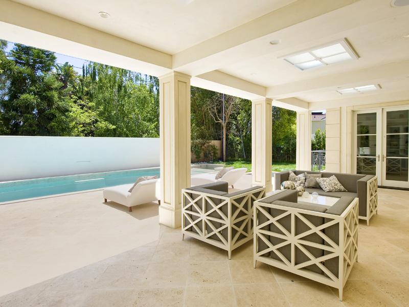 Covered patio with a view of the pool and metal armchairs and sofas with grey cushions in an LA mansion