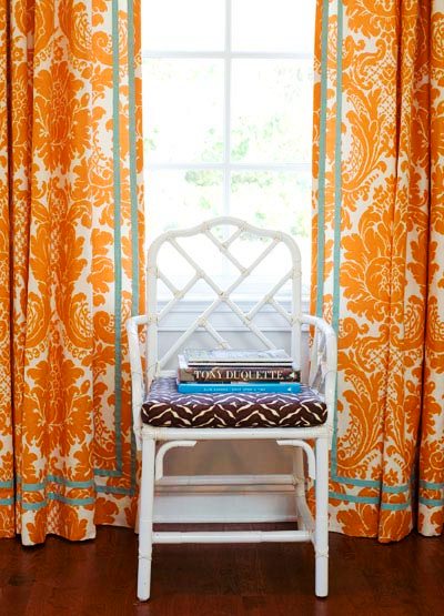 White glossy lacquer faux bamboo armchairs between orange and white brocade curtains in a cherry den