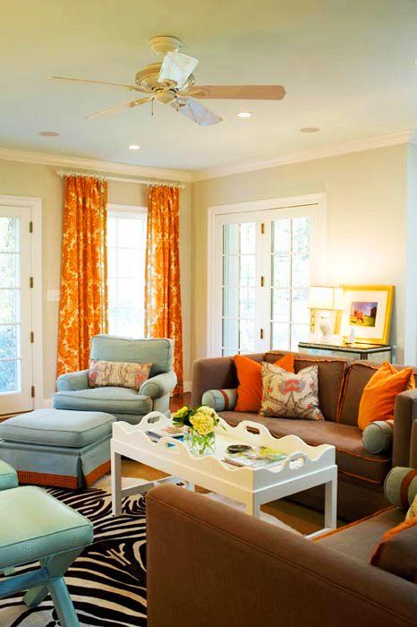 TV room with brown sofas, zebra print rug, orange and white brocade curtains, French doors, blue armchair with matching ottoman and two blue x-benches