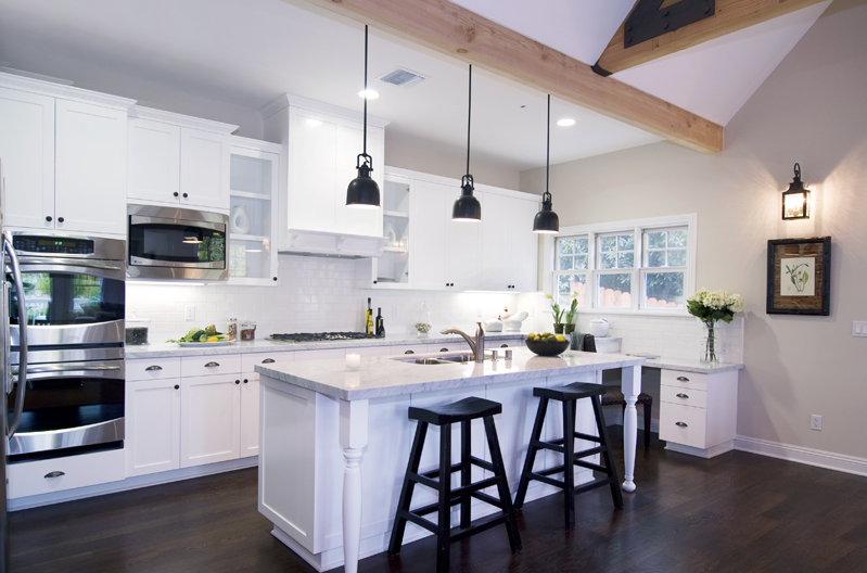 Kitchen in a modern farm house by Meredith Baer with three black pendant light, black barstools at a white island with a marble counter top, white cabinets and drawers and stainless appliances