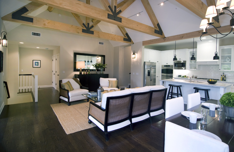 Living room in a modern farm house by Meredith Baer with truss-beamed ceiling, dark wood floor, white armchairs with wood arms and a matching sofa