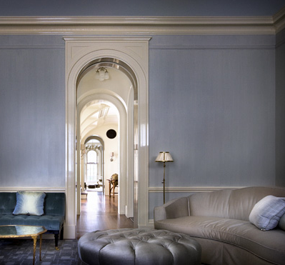 Grey sitting room in a New York brownstone by Peter Pennoyer with arched entryway, grey sofa, blue velvet tufted sofa and a round, grey, tufted ottoman