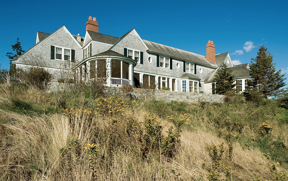 Traditional exterior of an East Coast waterfront home with gray shingle siding, black shutters and white trim by Peter Pennoyer