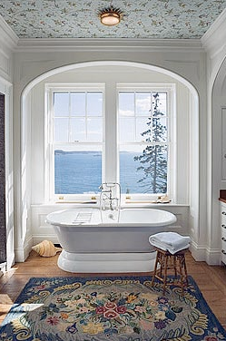 Master bathroom in an arched nook by Peter Pennoyer with a stand alone tub, view of the sea and a wallpapered ceiling