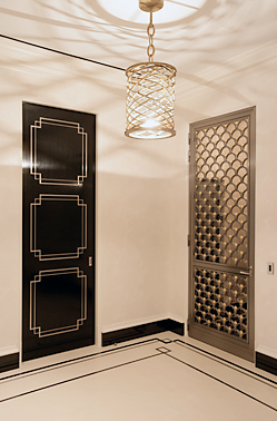 Park Avenue apartment foyer with white marble floors with black border and black door with white panel detail, an ornate screen door and a wiry pendant light by Peter Pennoyer