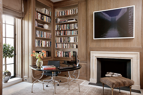 Library by Peter Pennoyer with wood paneled walls, built in bookshelves, a marble fireplace and metal and stone C-shaped table